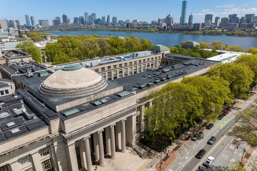 Aerial view of MIT’s Great Dome and campus in Cambridge, with the Charles River and the Boston skyline in the background.