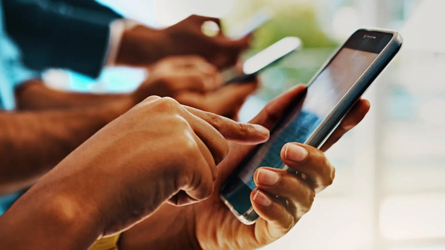 Close-up of several people’s hands holding and tapping on smartphones.
